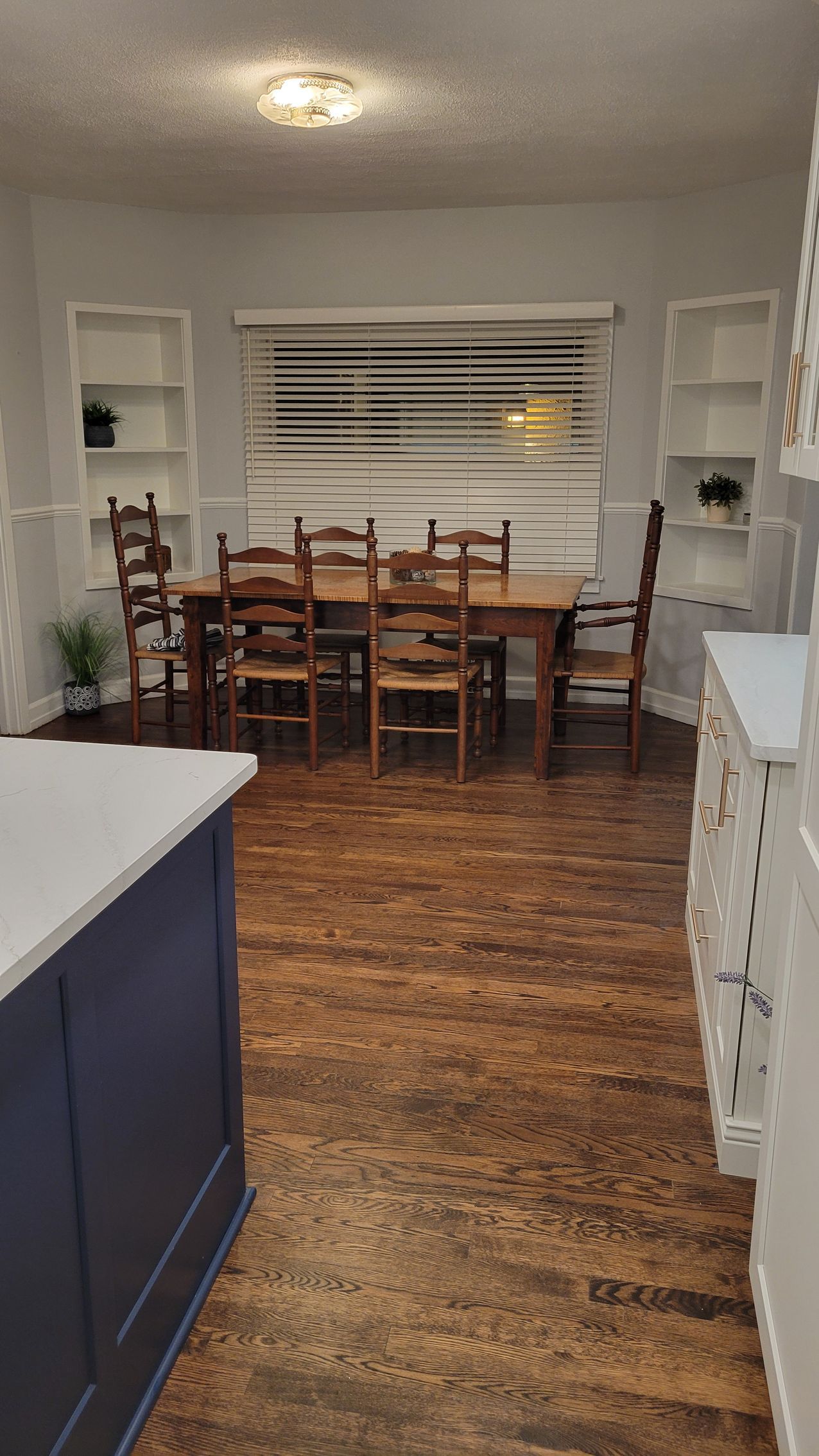 Dining room with wooden table and chairs, white shutters, and kitchen counters on either side.