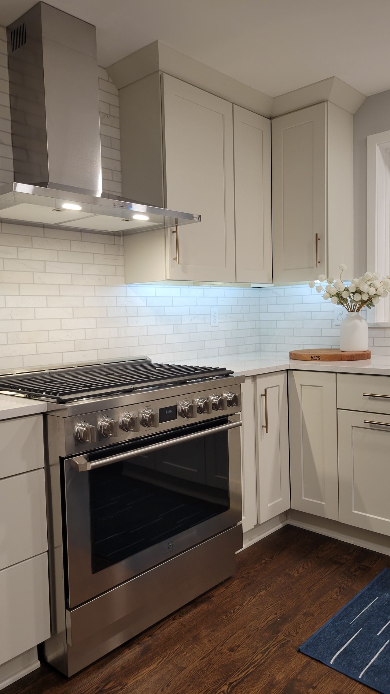 Modern kitchen with stainless steel stove, white cabinets, tile backsplash, and dark wood floor