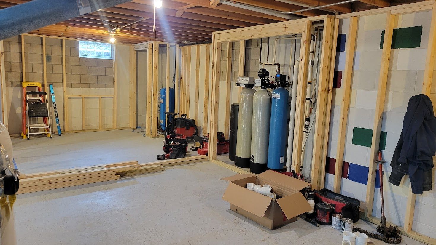 Unfinished basement with exposed studs, furnace and water heater, ladder, tools, and boxes on the floor