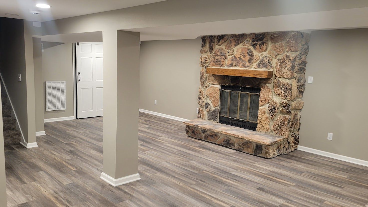 Empty living room with gray wood floors, stone fireplace, and open doorway.
