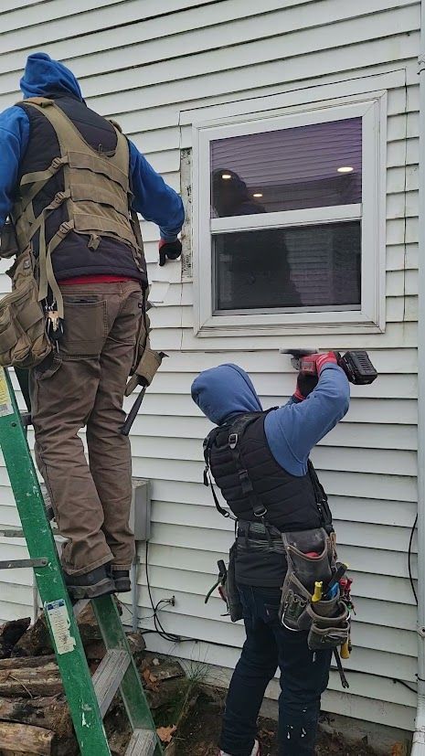 Two workers on a ladder installing siding around a house window