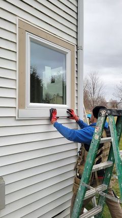 Person on ladder cleaning a house window with a cloth and spray bottle