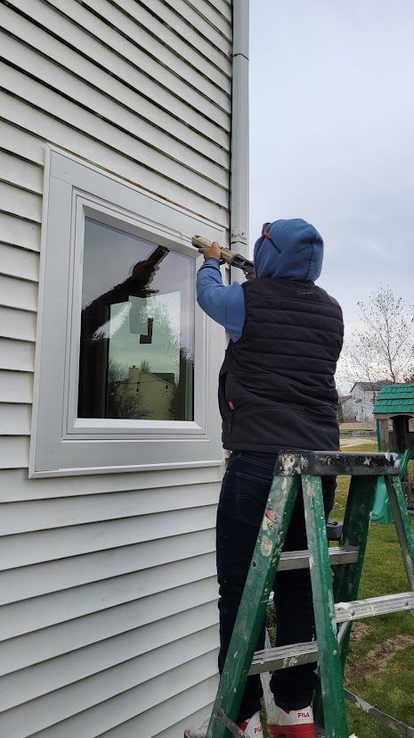 Worker on a ladder caulking around a window on a house exterior