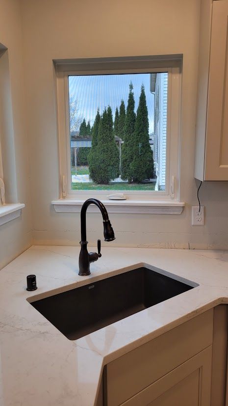 Bright kitchen sink and countertop beneath a window overlooking trees