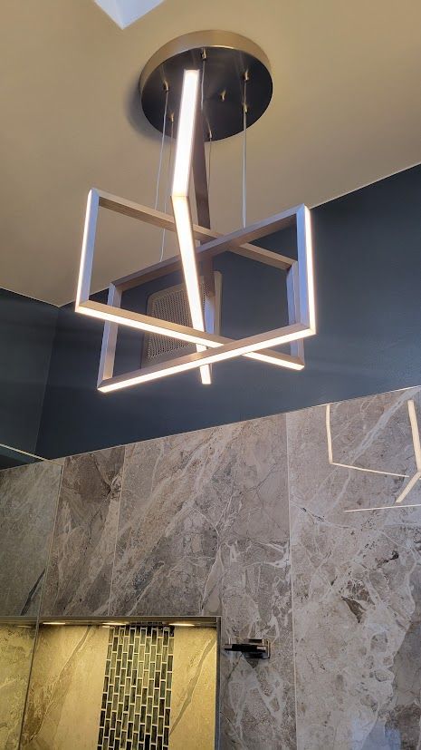 Modern geometric pendant light with glowing square frame above a gray marble wall and doorway