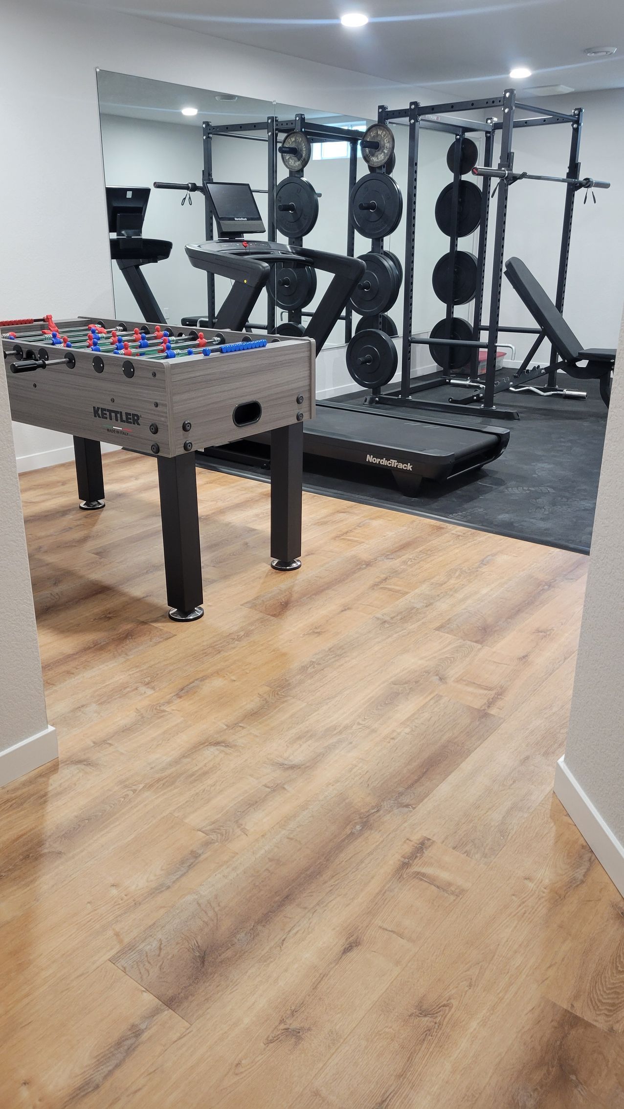 Home gym with weight rack, bench, and foosball table on wood flooring