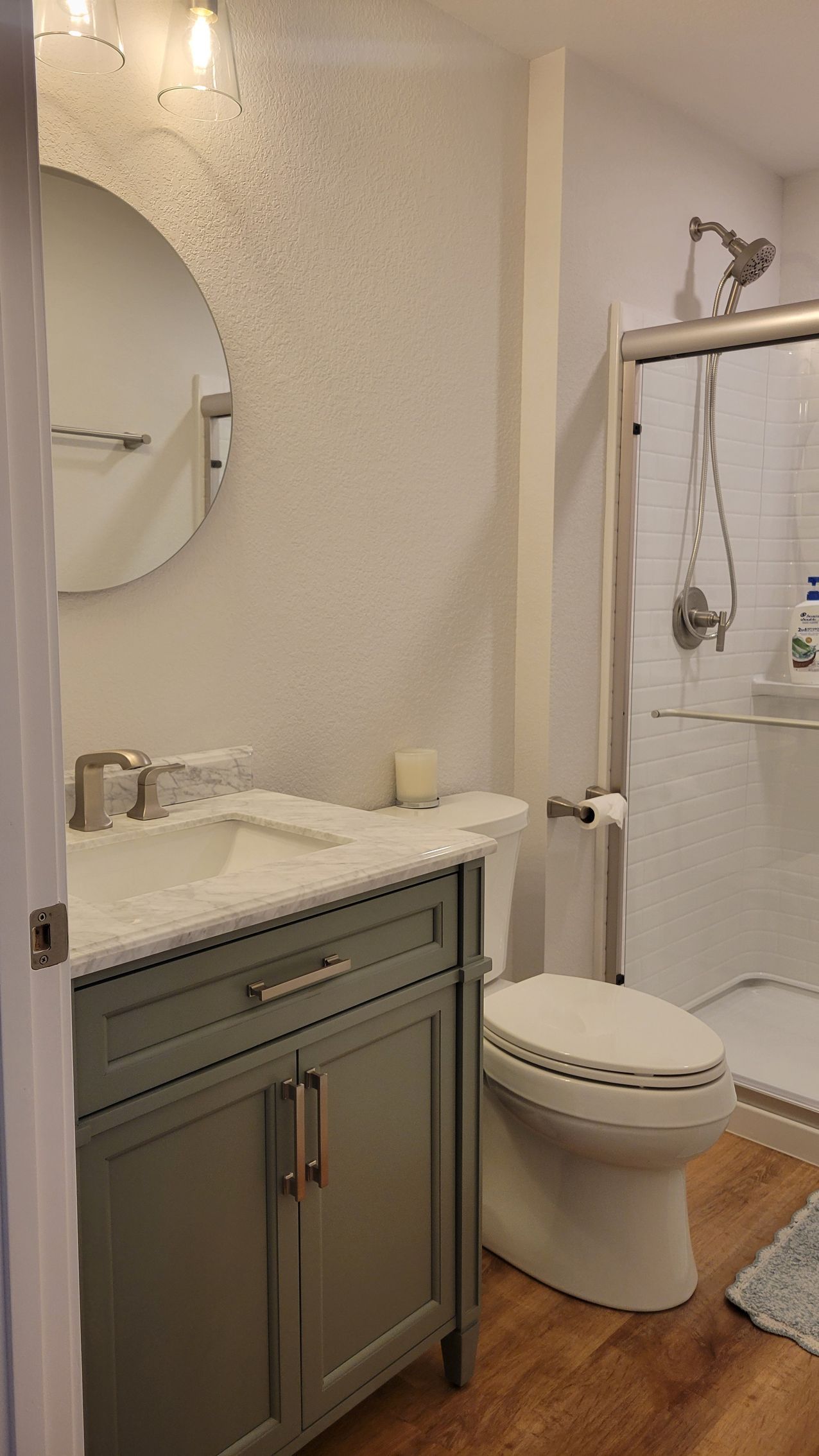 Small bathroom with gray vanity, round mirror, toilet, and walk-in shower with a white curtain.