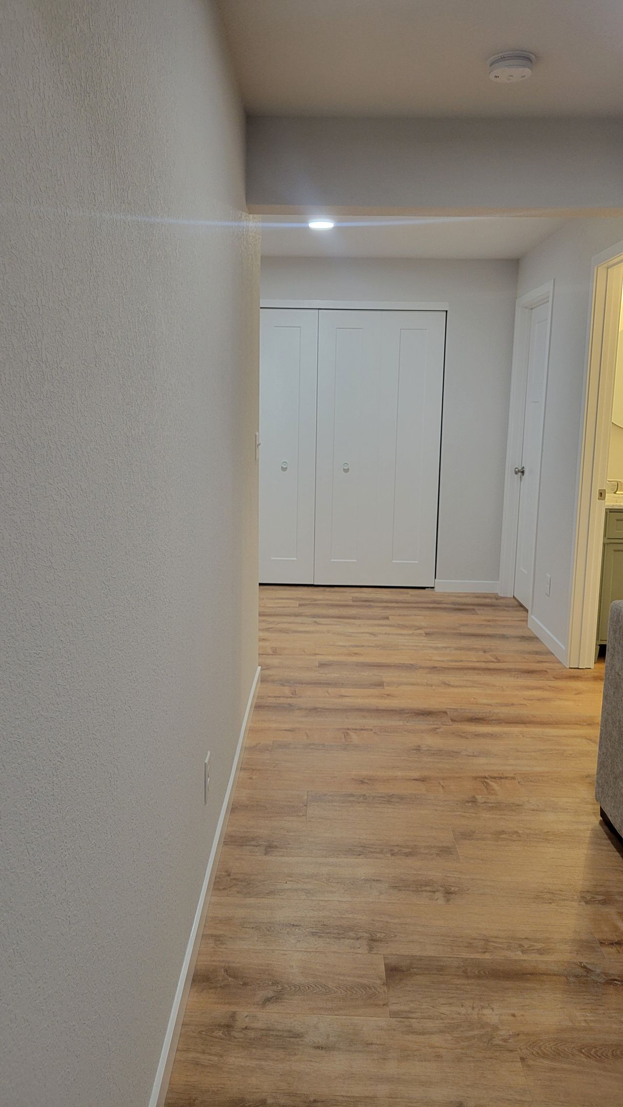 Hallway with wood floor, white closet doors, and a glimpse of a yellow shelf on the right.