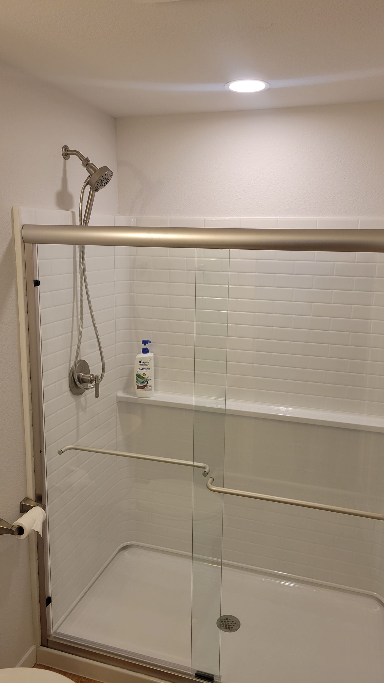 Walk-in shower with clear glass, white tile walls, and a handheld showerhead.