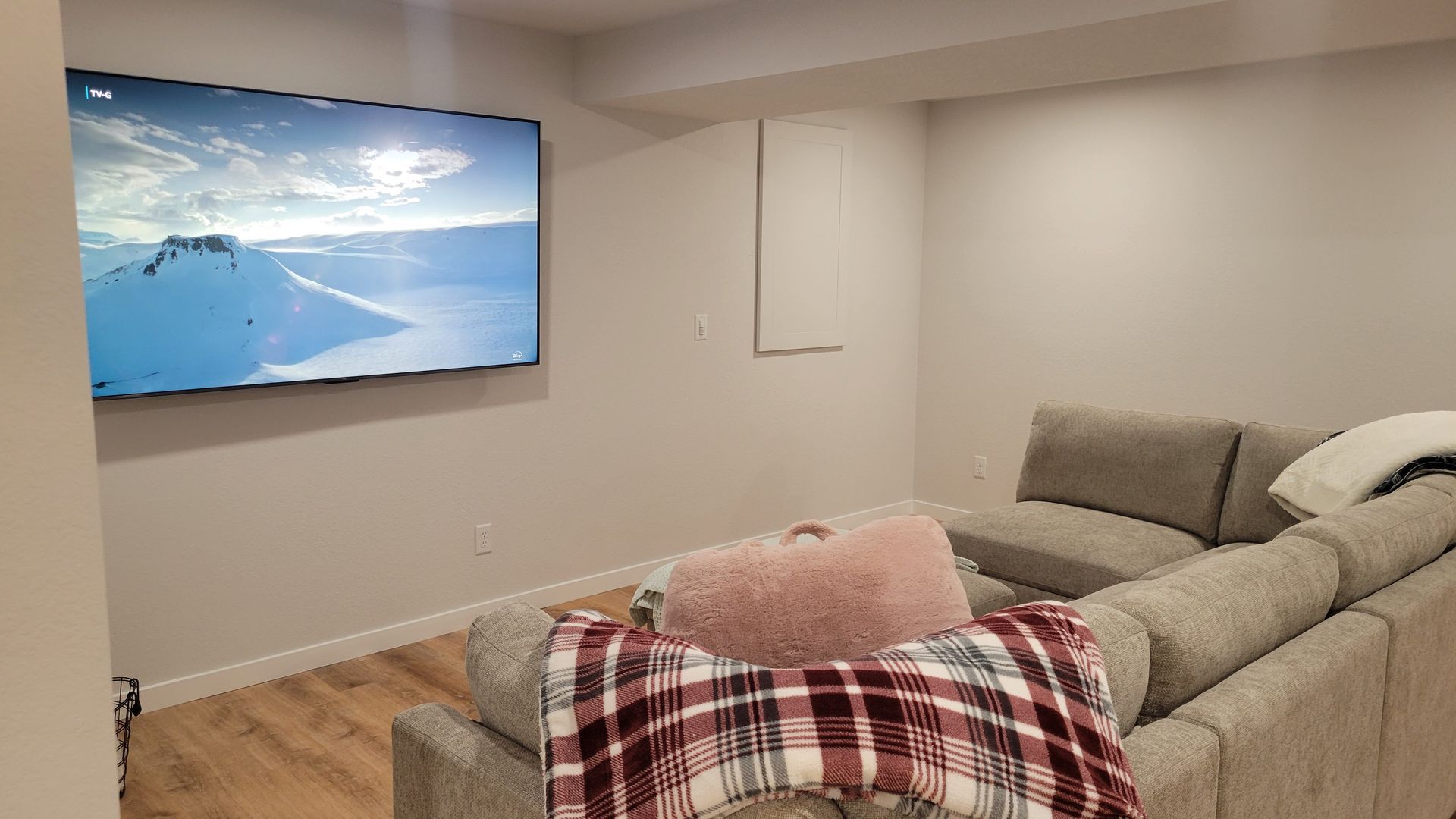 Cozy living room with wall-mounted TV, gray sectional sofa, and a plaid blanket on the ottoman.