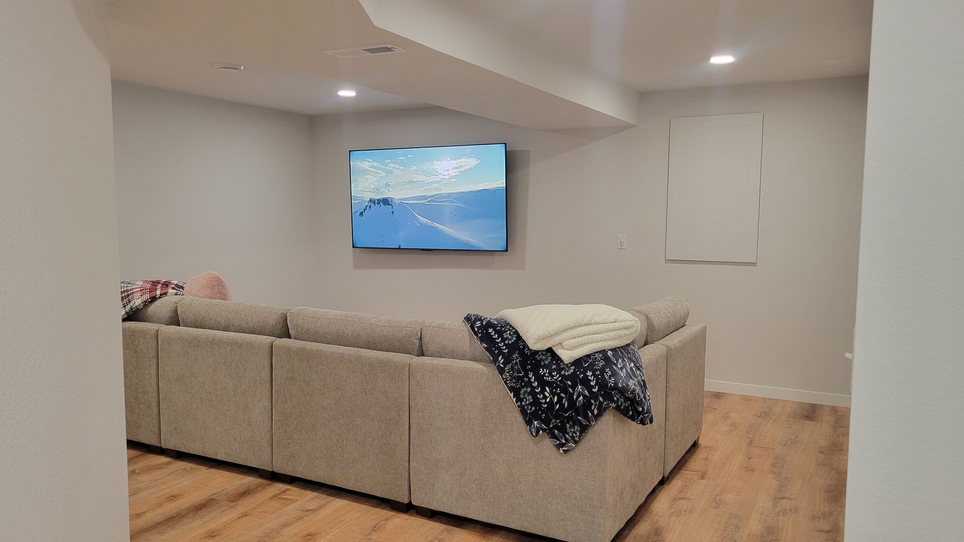 Modern living room with a gray sectional sofa, wall-mounted TV, and hardwood floors