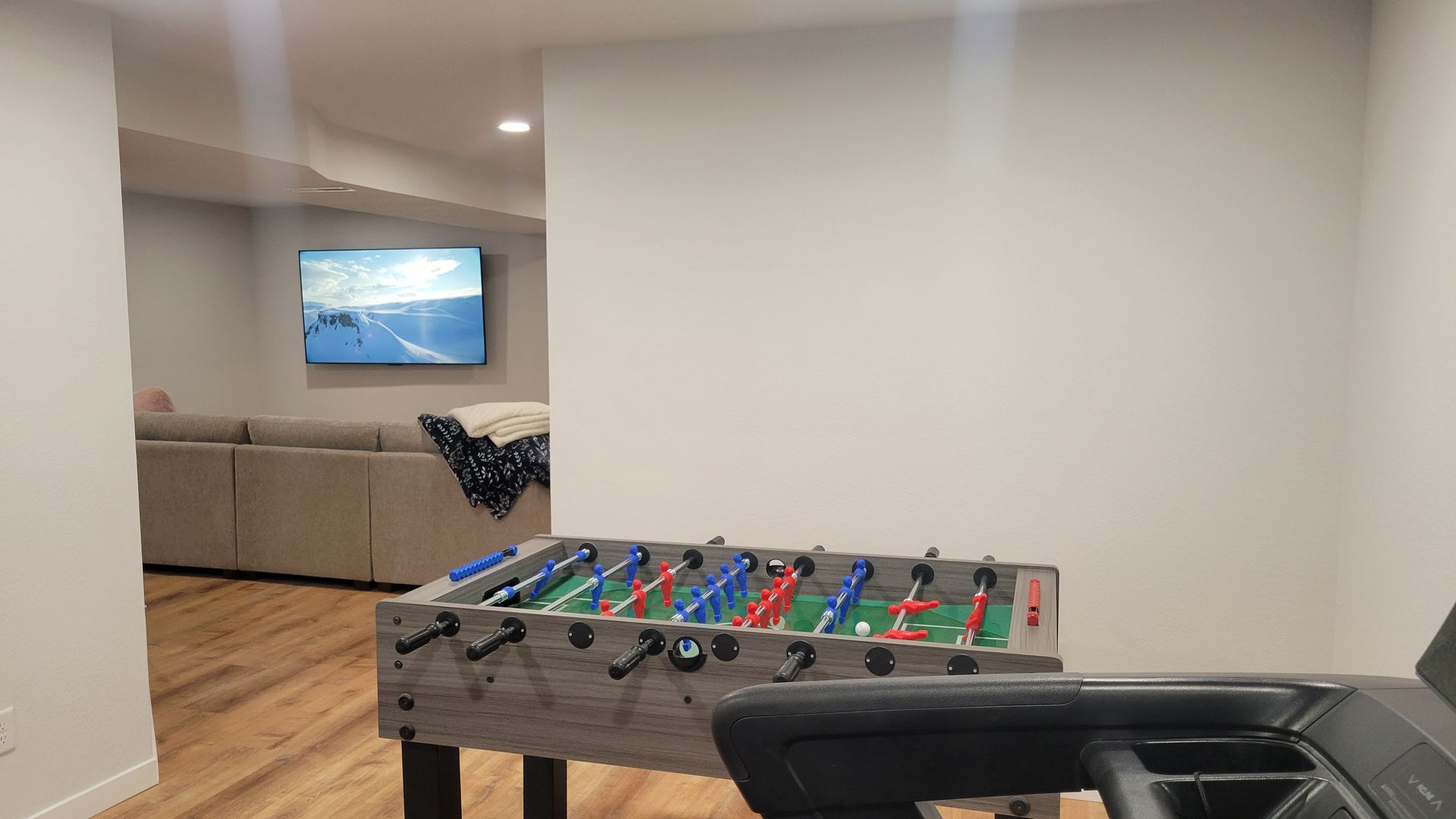 Game room with foosball table, black seating, wood floor, and a TV in the adjacent living area