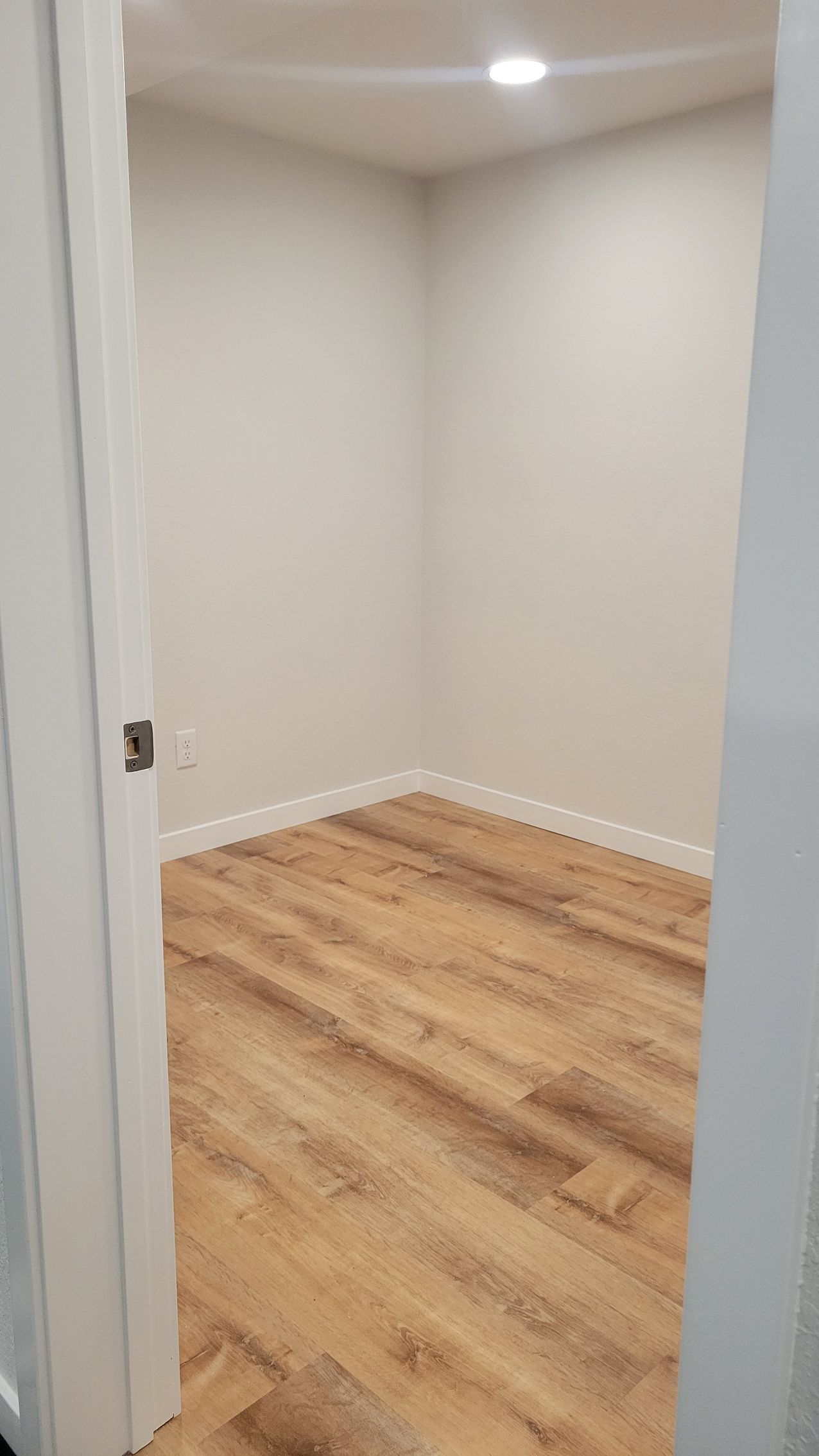 Empty beige room with wood flooring and white trim, viewed through an open doorway