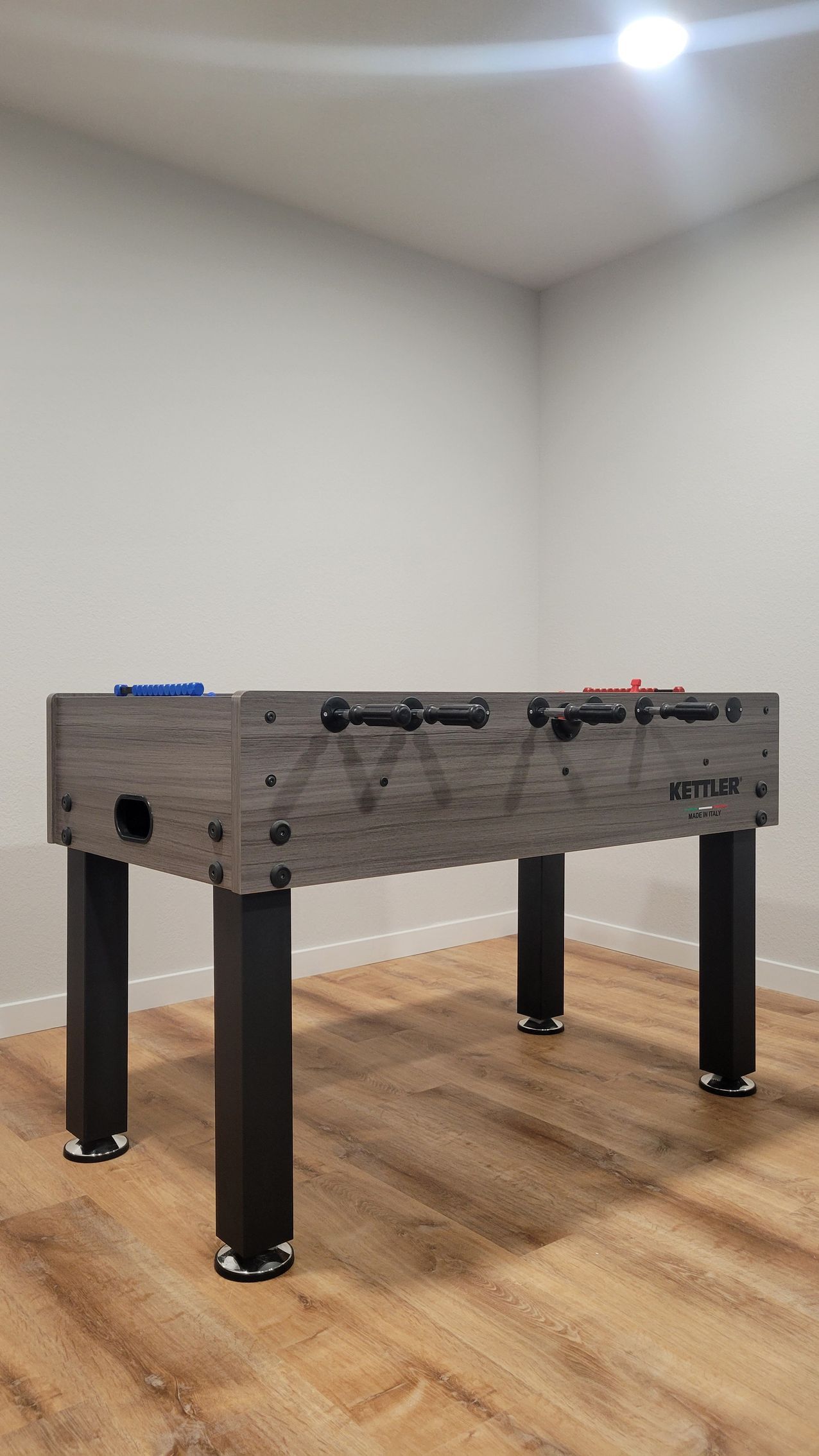 Foosball table in a bare room with wood floor and white walls