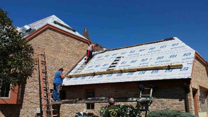 Workers installing roofing underlayment on a brick house roof