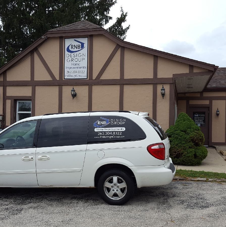 White minivan parked in front of a tan business building with a sign above the entrance.