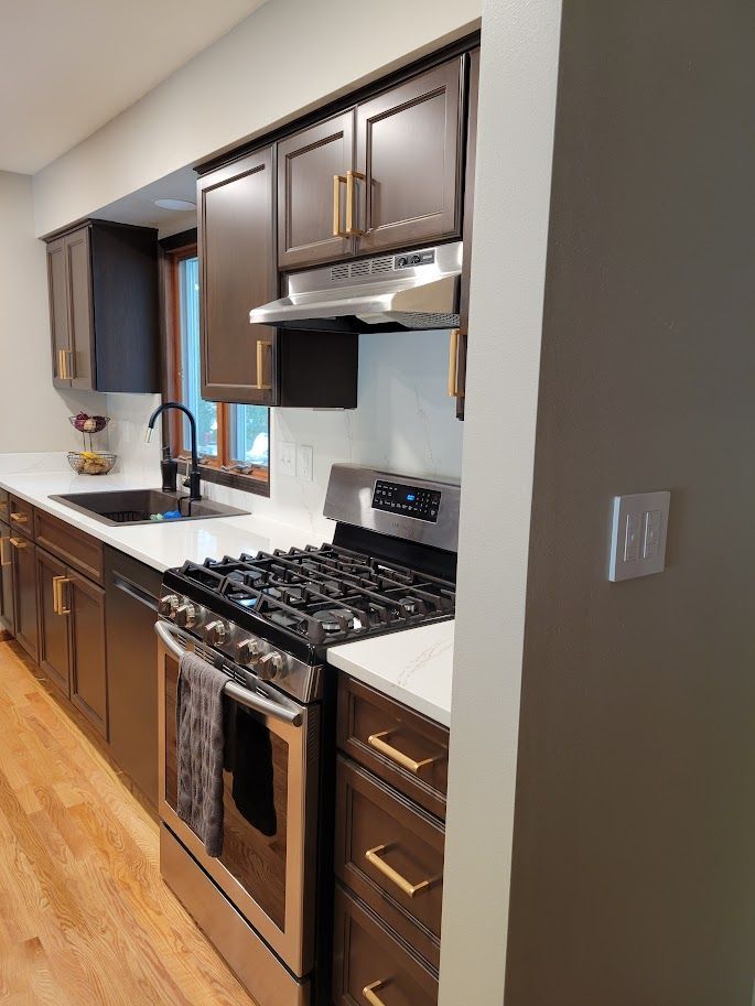 Modern kitchen with dark cabinets, stainless steel stove, white countertops, and hardwood floors.