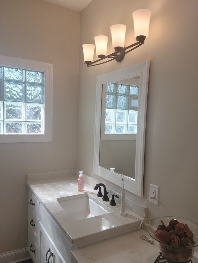 Bright bathroom vanity with white sink, mirror, wall sconce, and frosted windows