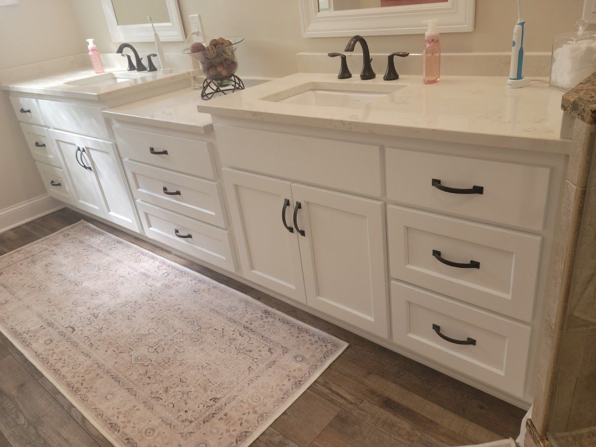 Bright bathroom vanity with white cabinets, black faucets, and a beige countertop beside a patterned rug.