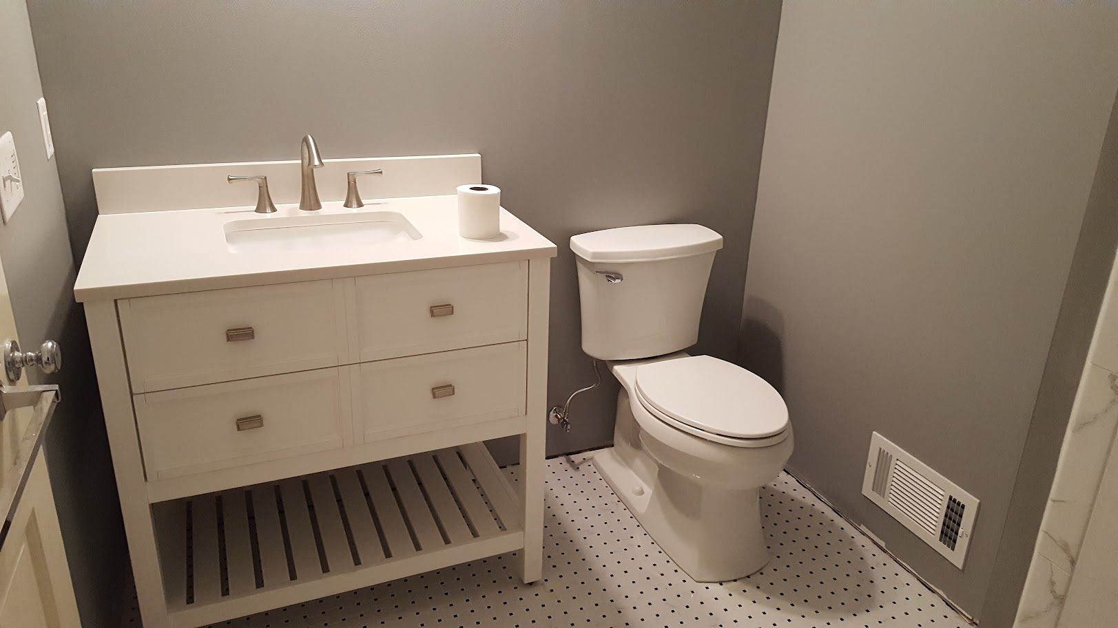 Small bathroom with white vanity, toilet, and gray walls with patterned floor tiles.