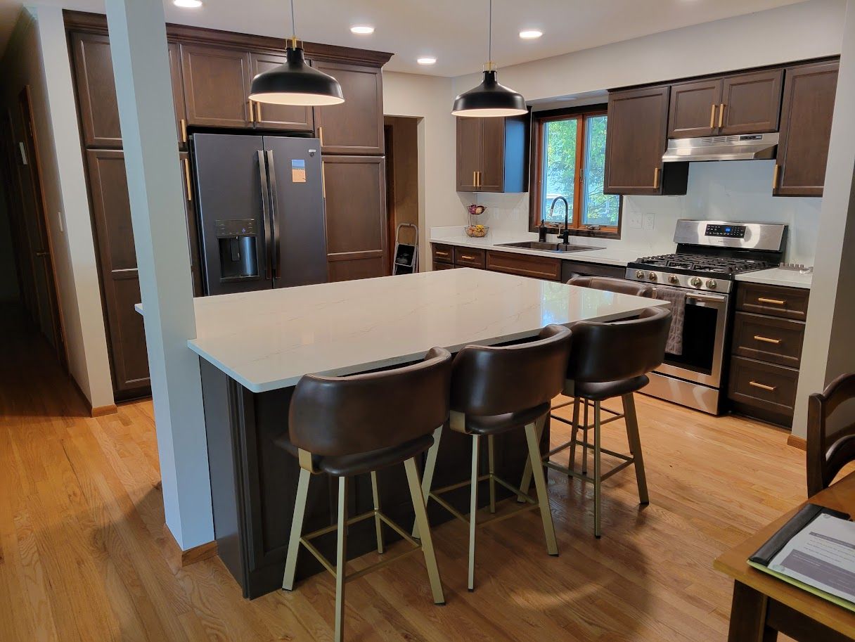 Modern kitchen with a large island, dark cabinets, stainless appliances, and three barstools
