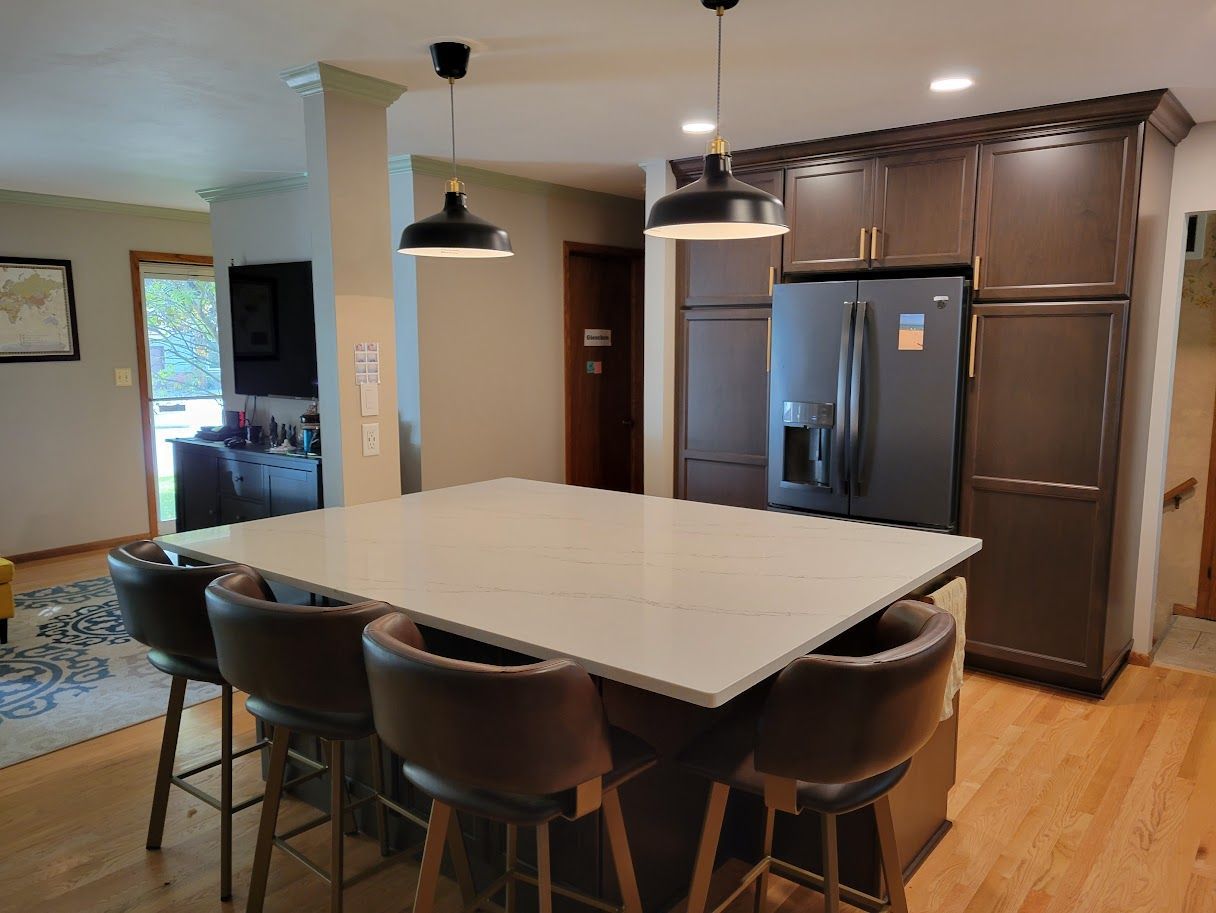 Modern kitchen with large island, pendant lights, barstools, stainless steel fridge, and hardwood floors