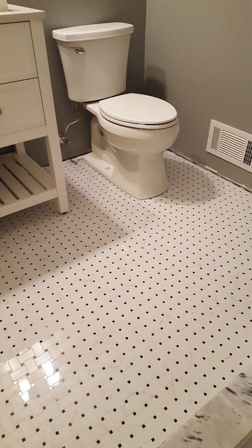 Small bathroom with white toilet, dotted tile floor, vanity edge, and wall vent.