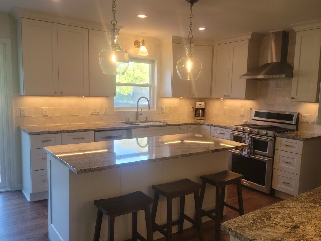 Bright modern kitchen with white cabinets, granite island, pendant lights, and stainless steel appliances