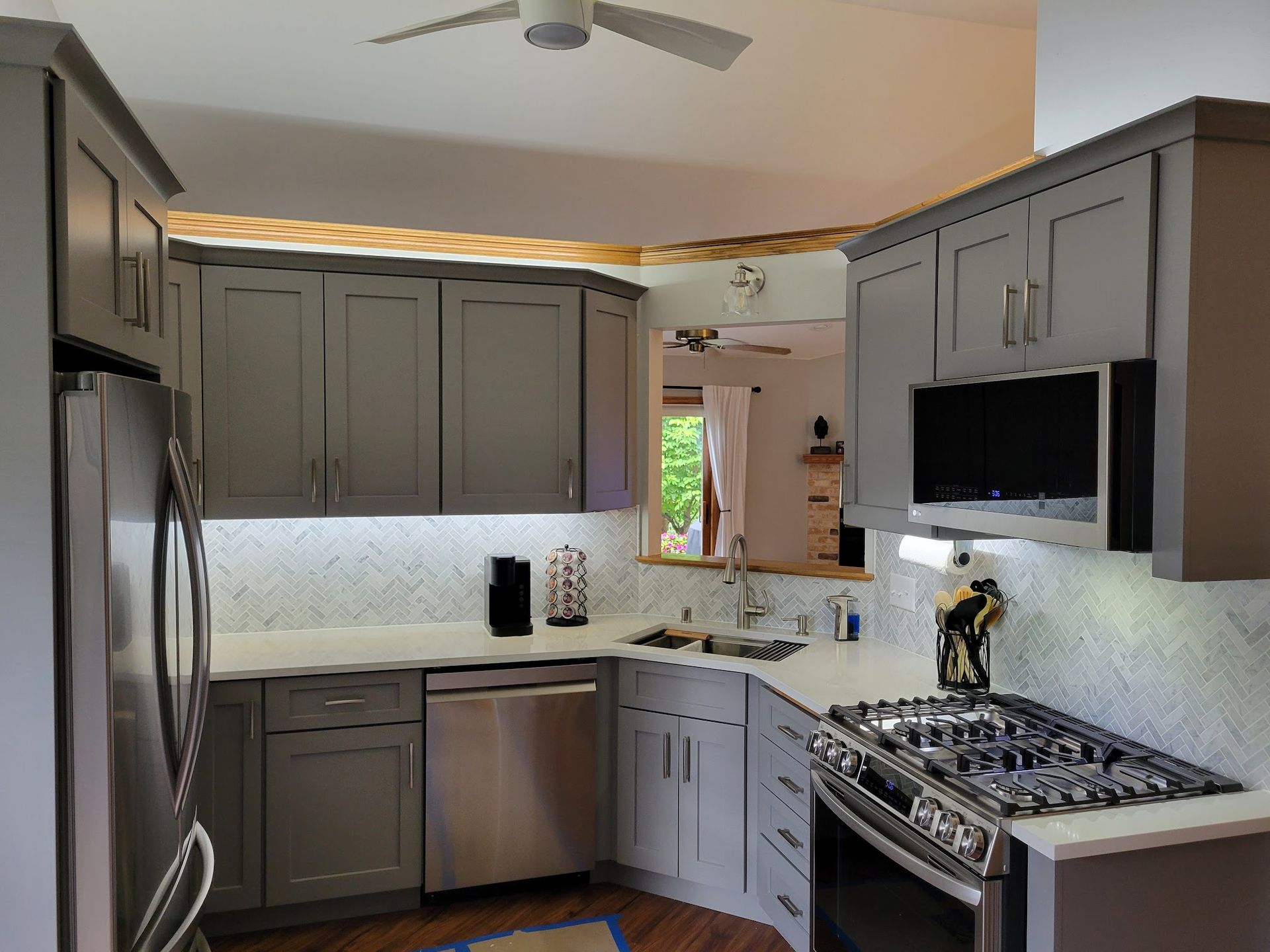 Modern gray kitchen with stainless steel appliances, gas stove, white backsplash, and ceiling fan