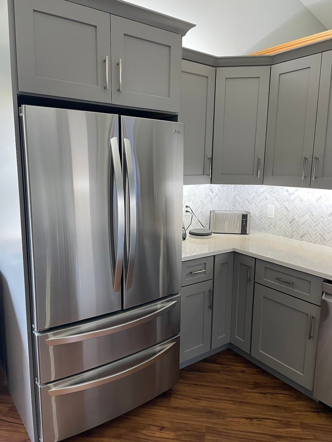 Modern kitchen with stainless steel refrigerator, gray cabinets, white countertops, and wood flooring