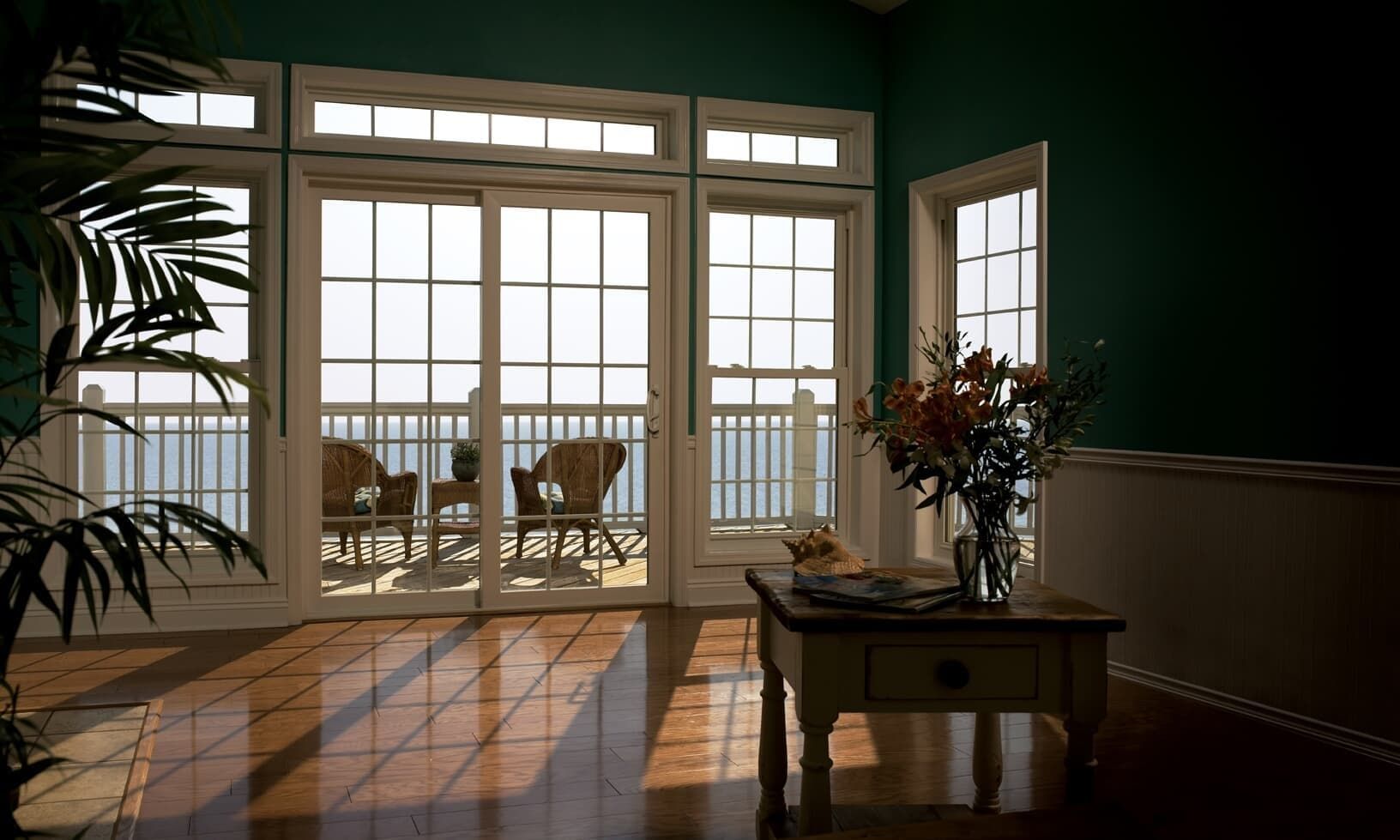 Sunlit room with French doors, balcony chairs, and a small table with flowers and a plant.