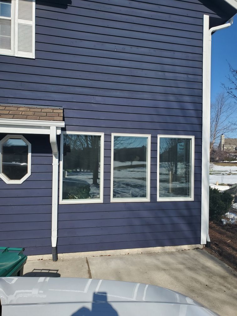 Blue house exterior with three windows, white trim, and a driveway in front