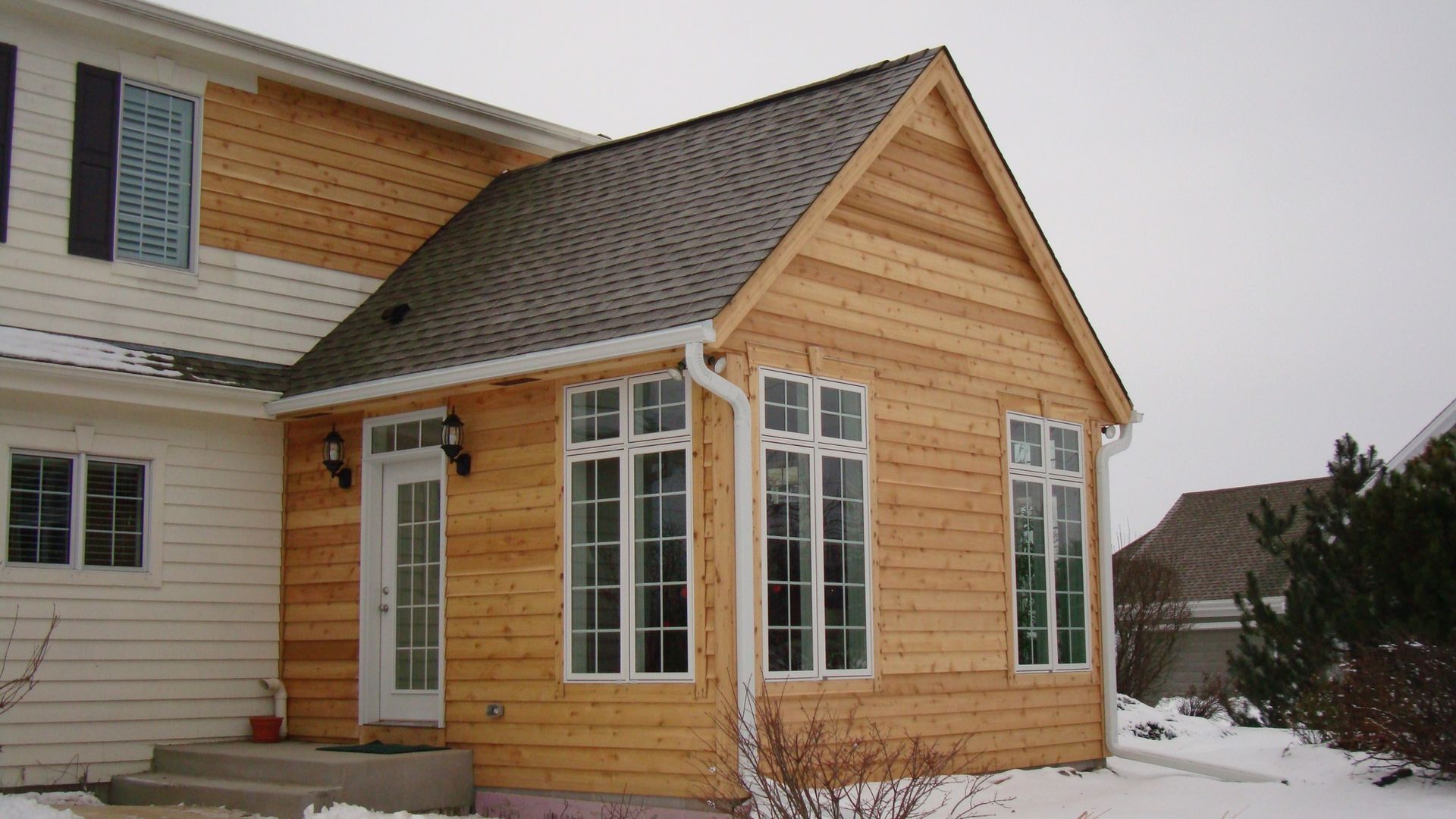Snowy tan and white house exterior with a side addition and large windows