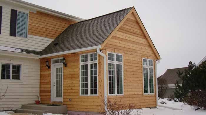 Snowy house exterior with tan siding, white trim, and a bay window extension