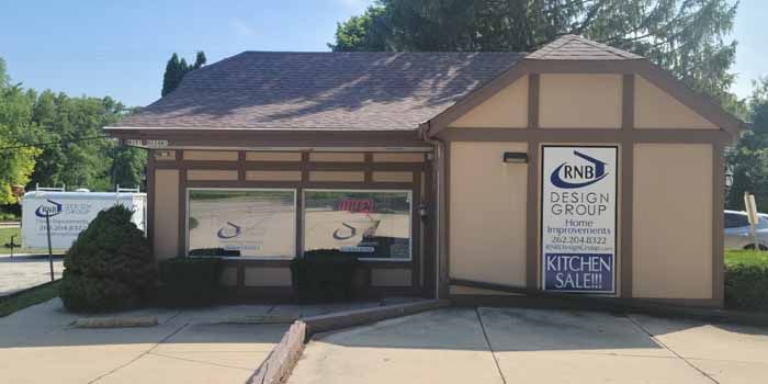 Small tan-and-brown commercial building with a large sign and a front entrance under a blue sky