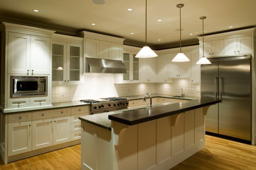 Modern white kitchen with island, pendant lights, stainless steel appliances, and hardwood floors