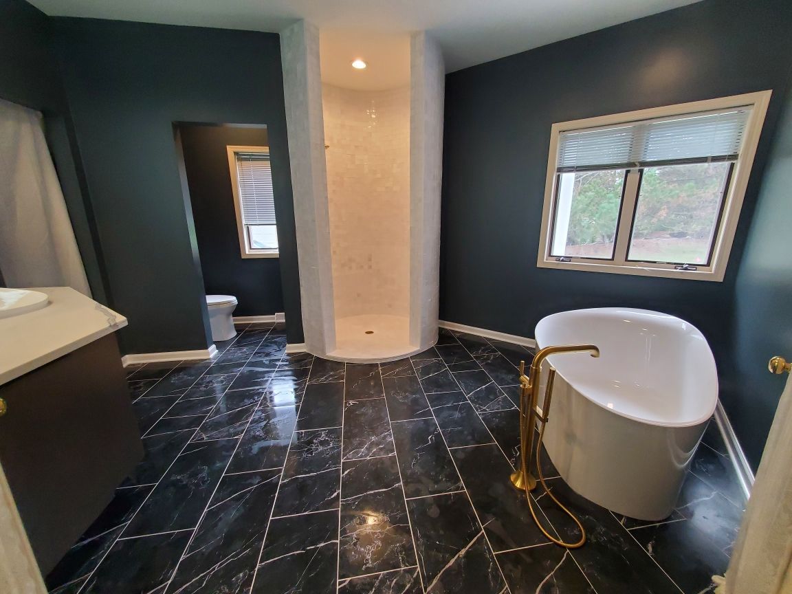 Modern bathroom with dark tile floor, freestanding tub, and window, still under construction
