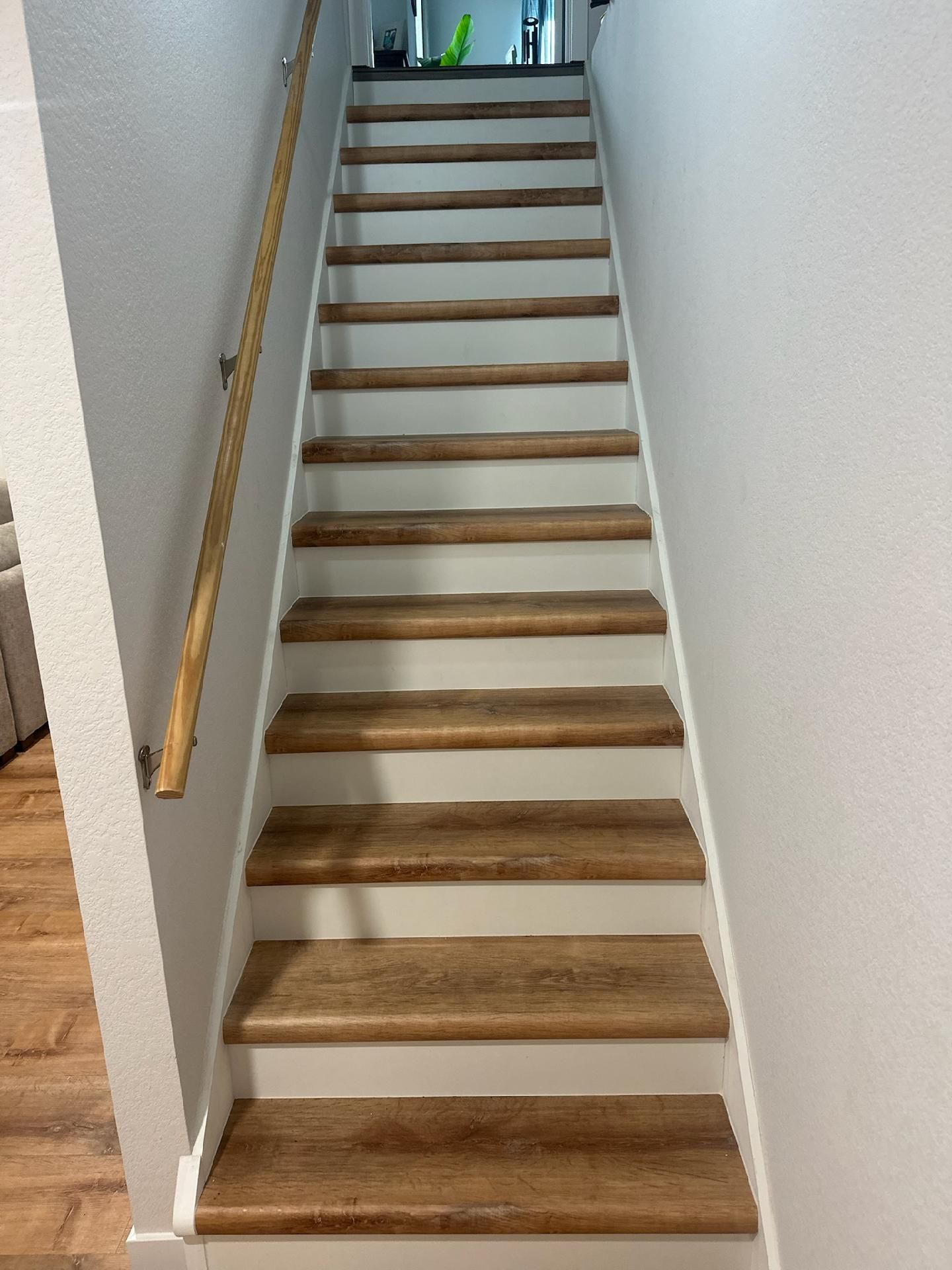 Narrow indoor staircase with wooden steps, white walls, and a metal handrail on the left