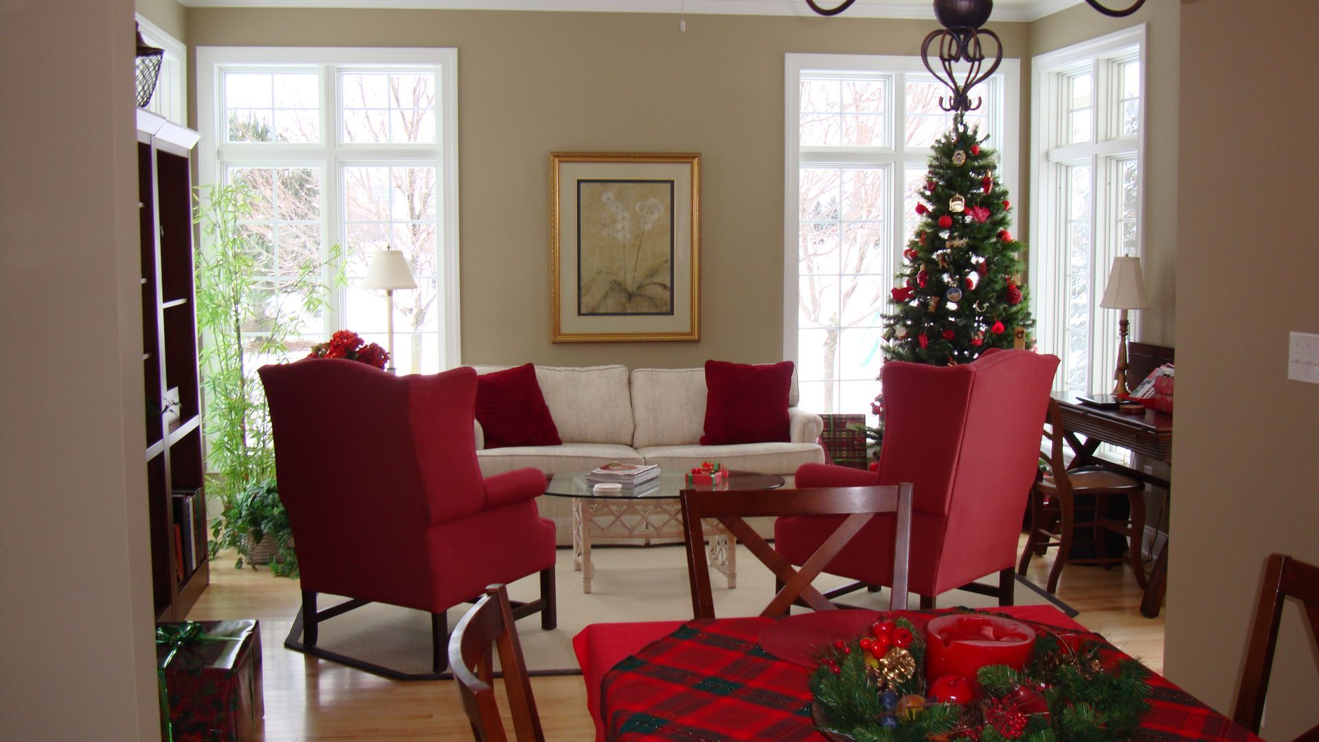Cozy living room with red chairs, white sofa, Christmas tree, and plaid holiday decor near large windows