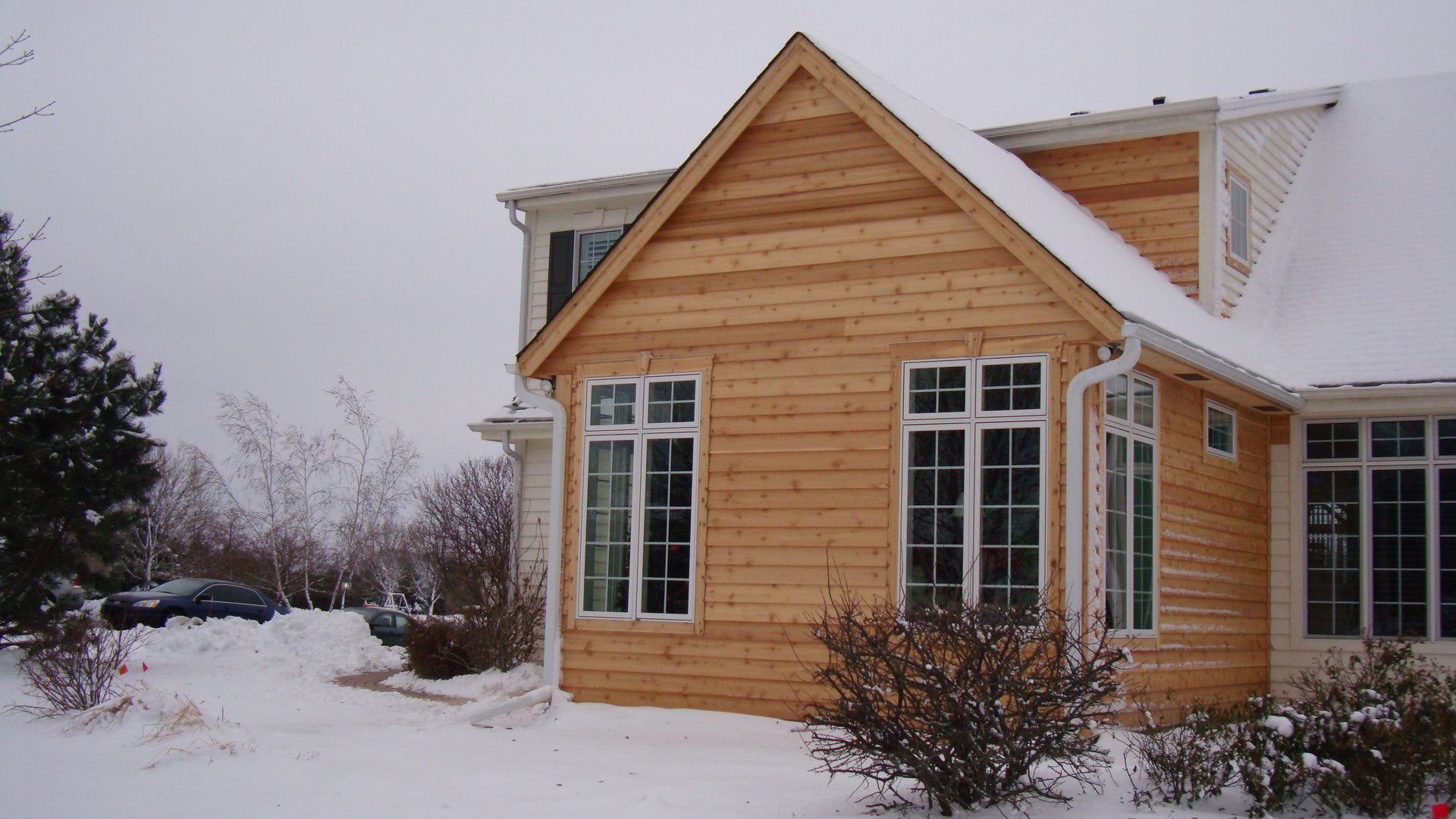 Snow-covered wooden house with white-trimmed windows on a cloudy winter day