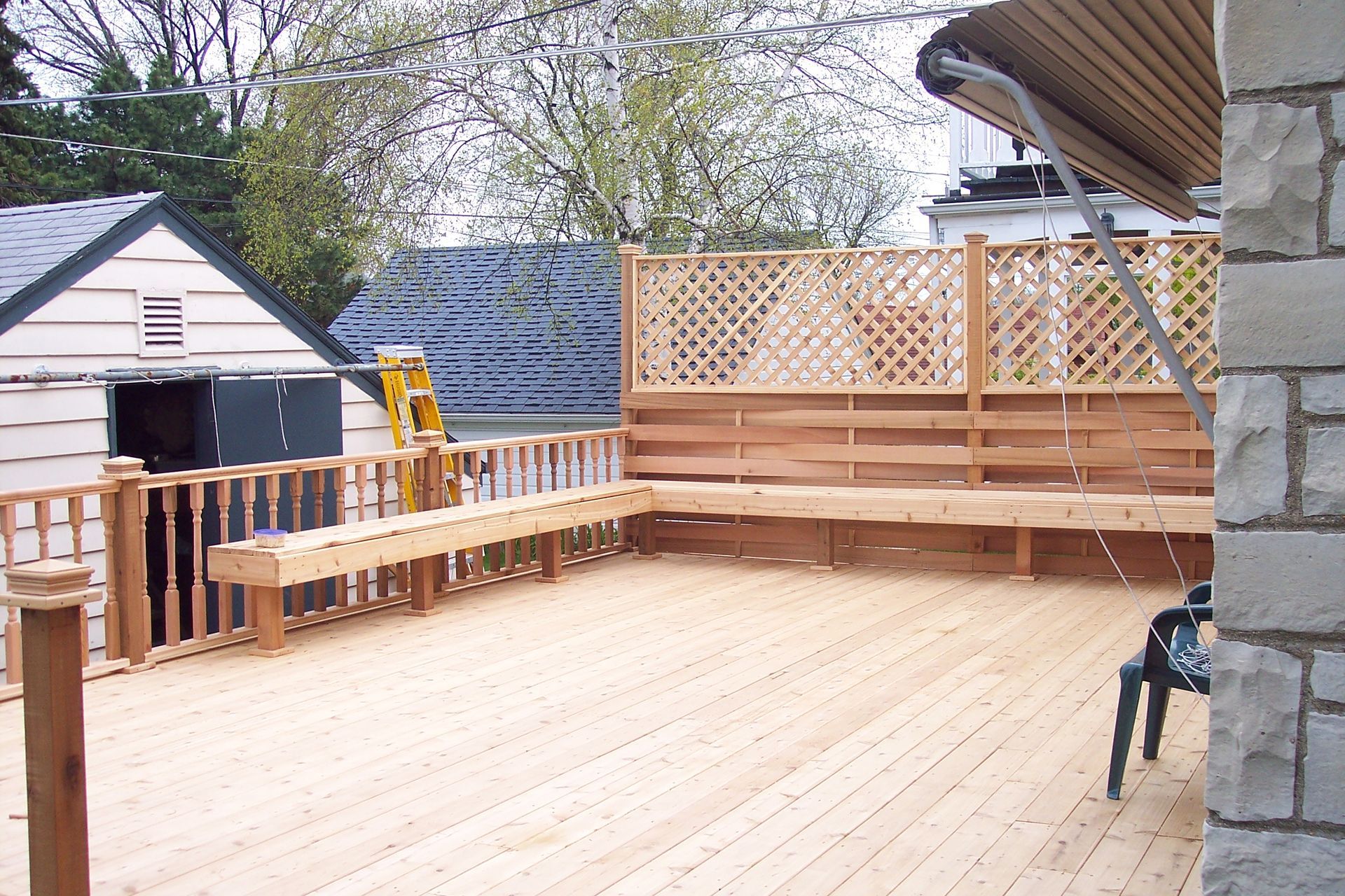 Wooden backyard deck with benches and lattice railing beside a house, viewed in daylight