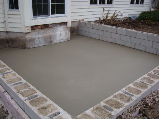Freshly poured concrete patio beside a house with stone retaining walls