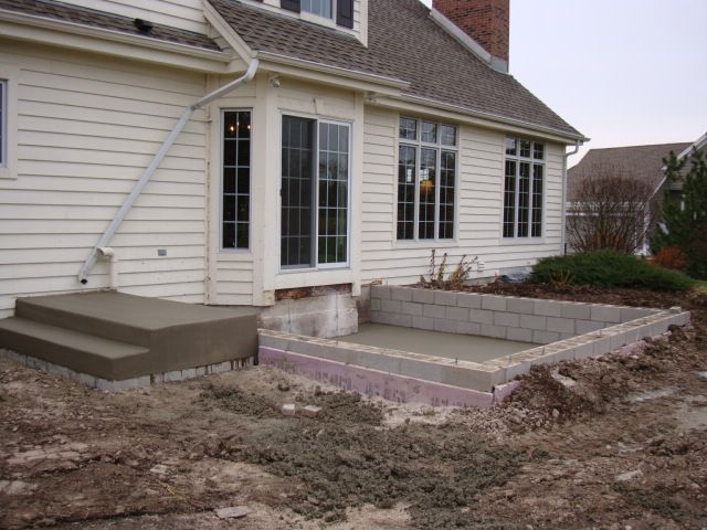 House exterior with unfinished concrete patio and steps in a muddy yard