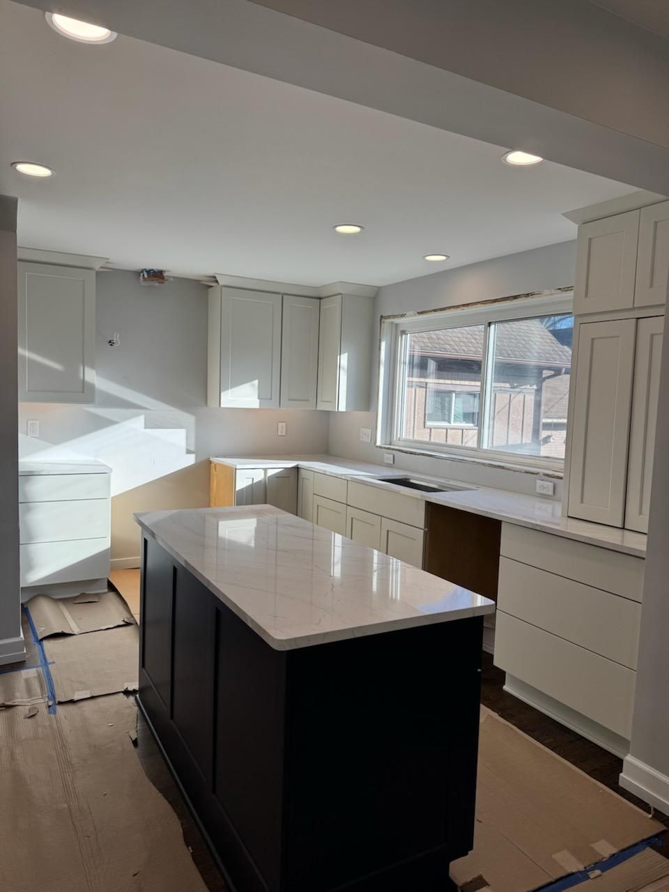 Bright modern kitchen with white cabinets, black island, and large window over the sink.