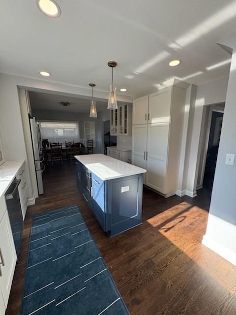 Bright kitchen with blue island, white cabinets, dark wood floor, and dining area in the background.
