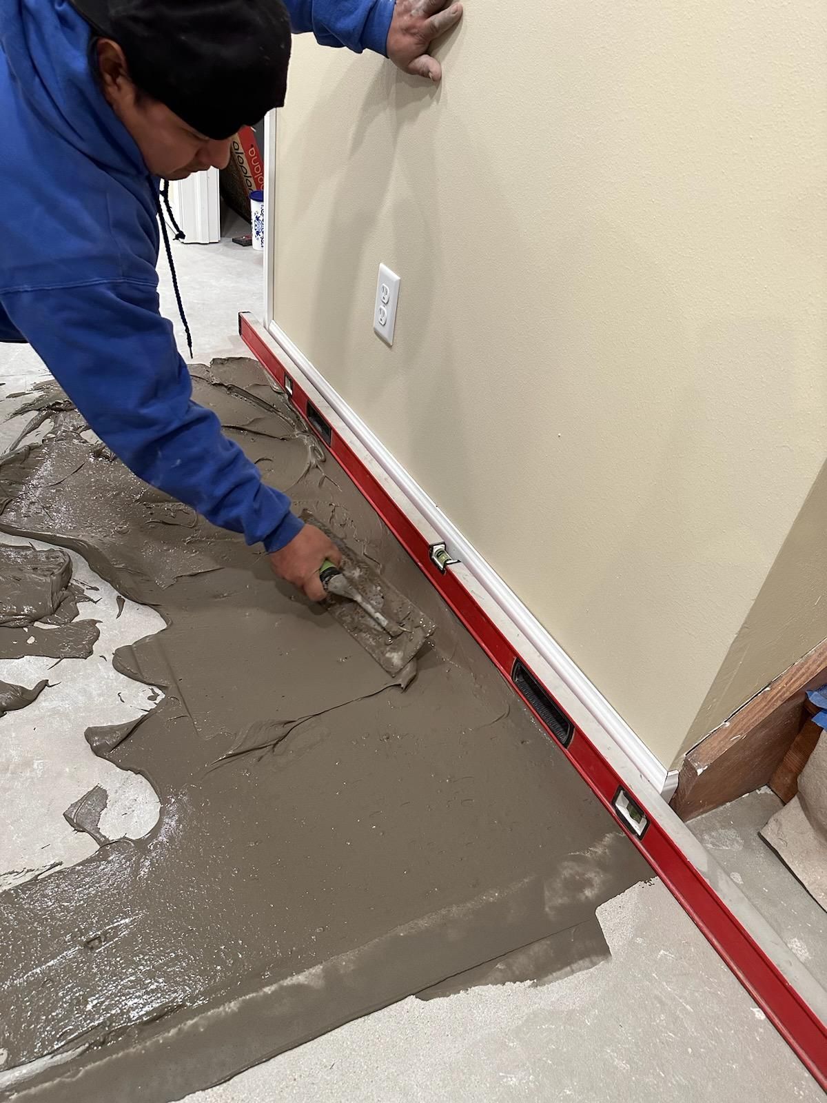 Worker smoothing wet concrete along a wall with a trowel and red edging strip