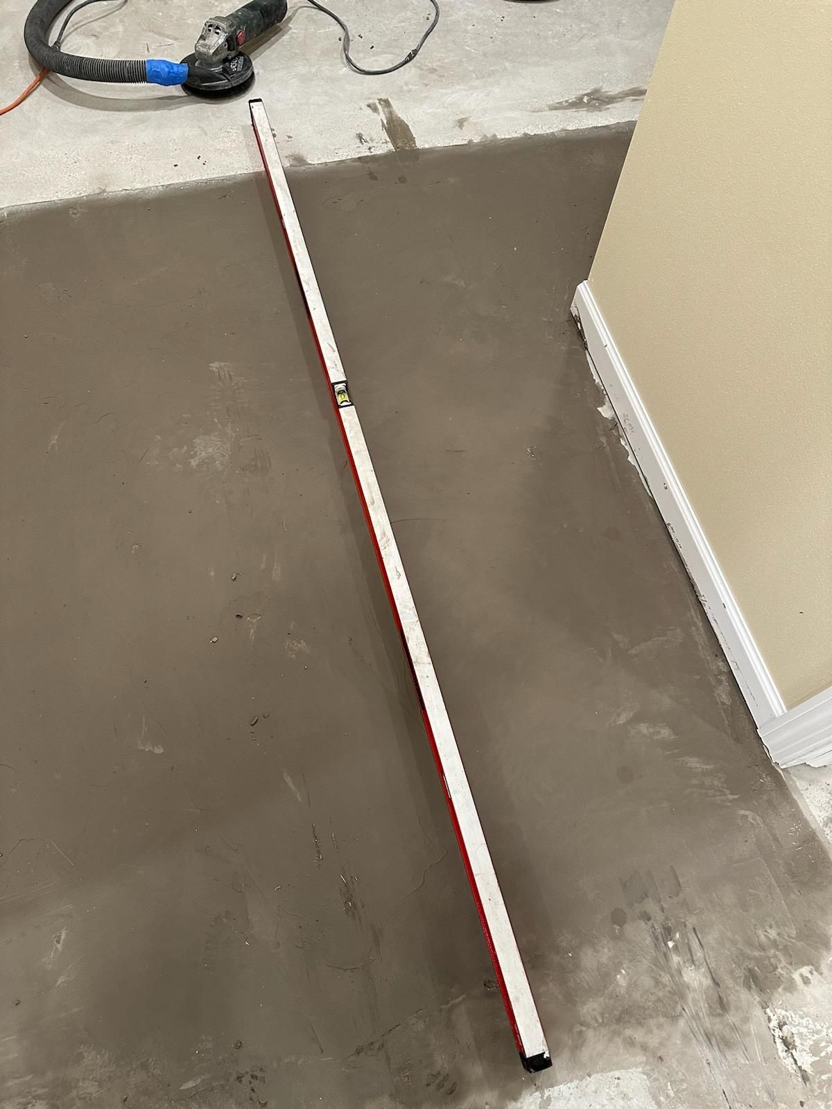 Freshly smoothed gray floor with a red-and-white pole and power tool on the concrete edge