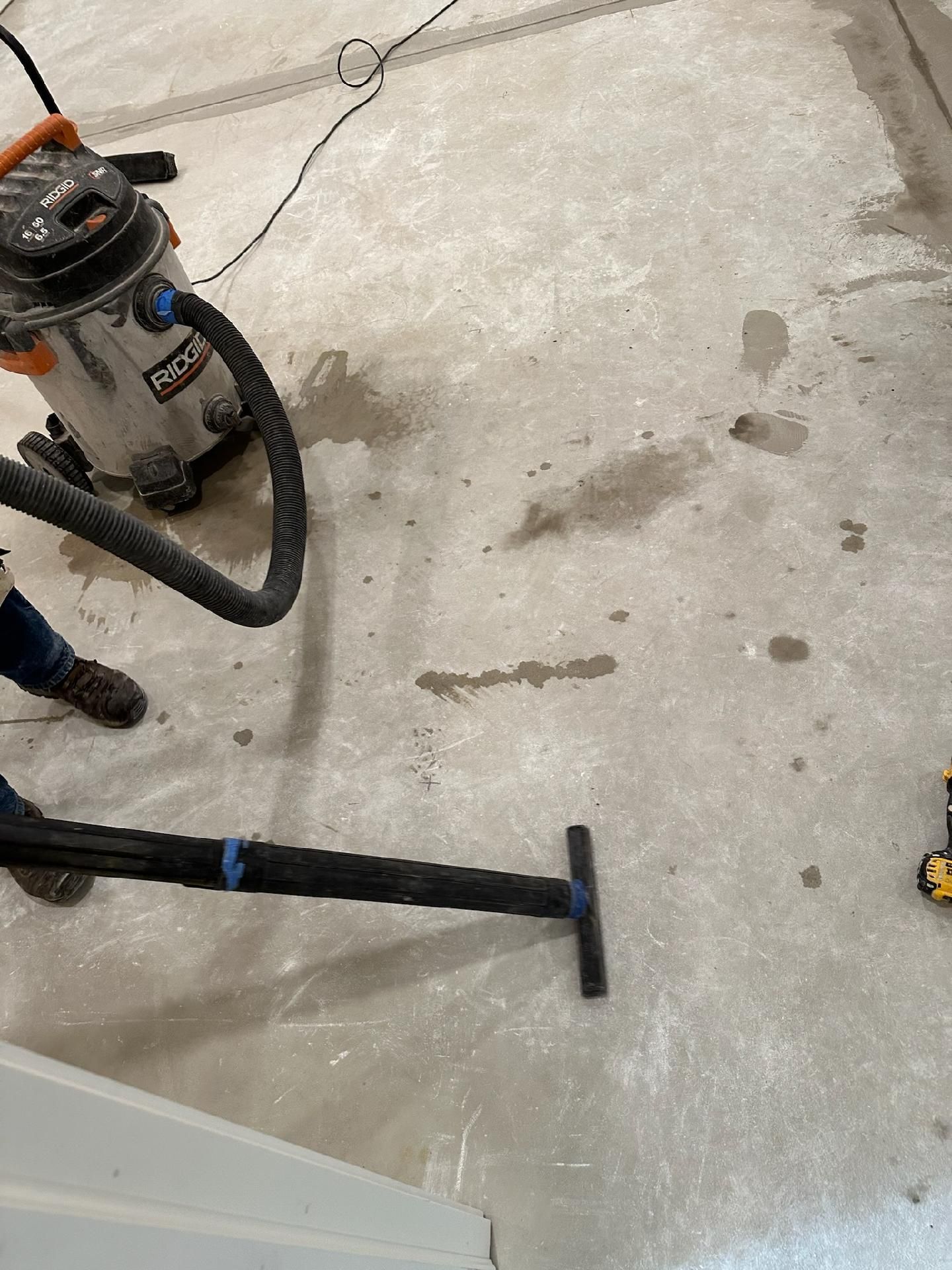 Concrete floor with a shop vacuum and a dust mop in a garage or workshop.