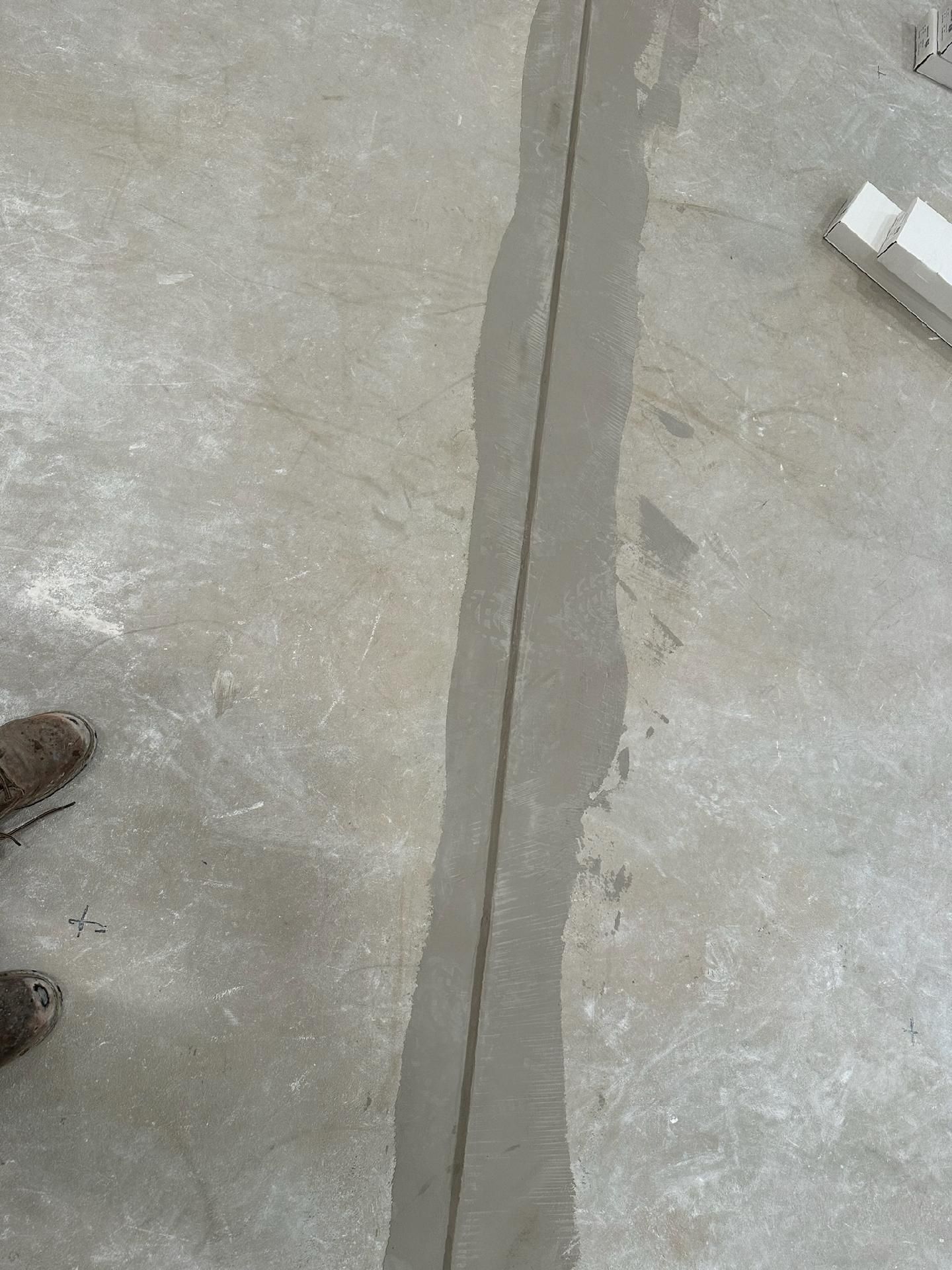 Cracked concrete floor with a long seam; shoes visible at the lower left and a small white object at the upper right