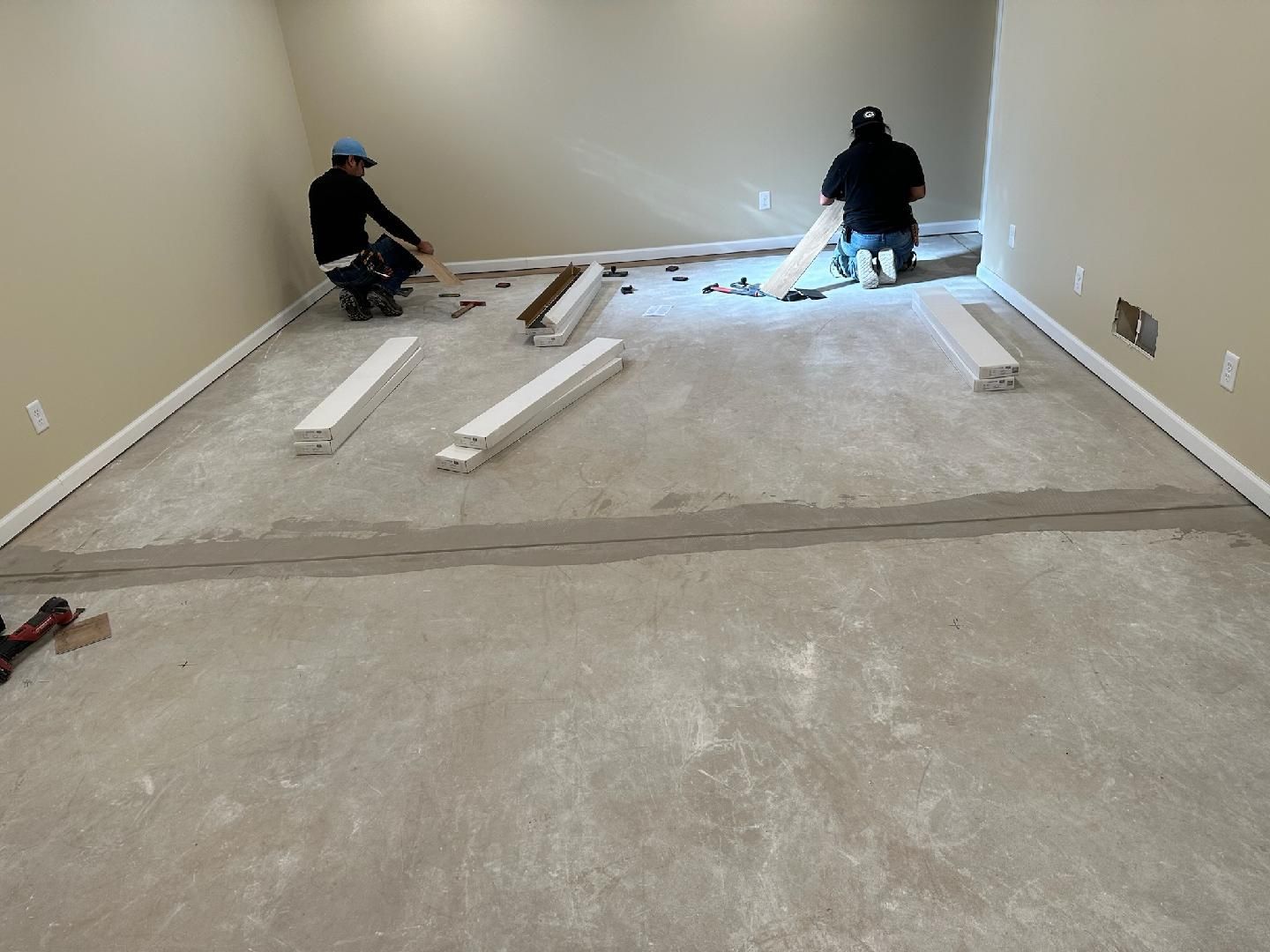 Workers installing flooring in an empty room with white walls and construction materials scattered on the floor